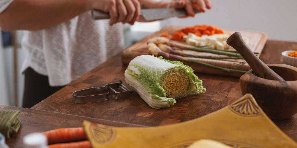 person slicing green vegetable on brown wooden chopping board